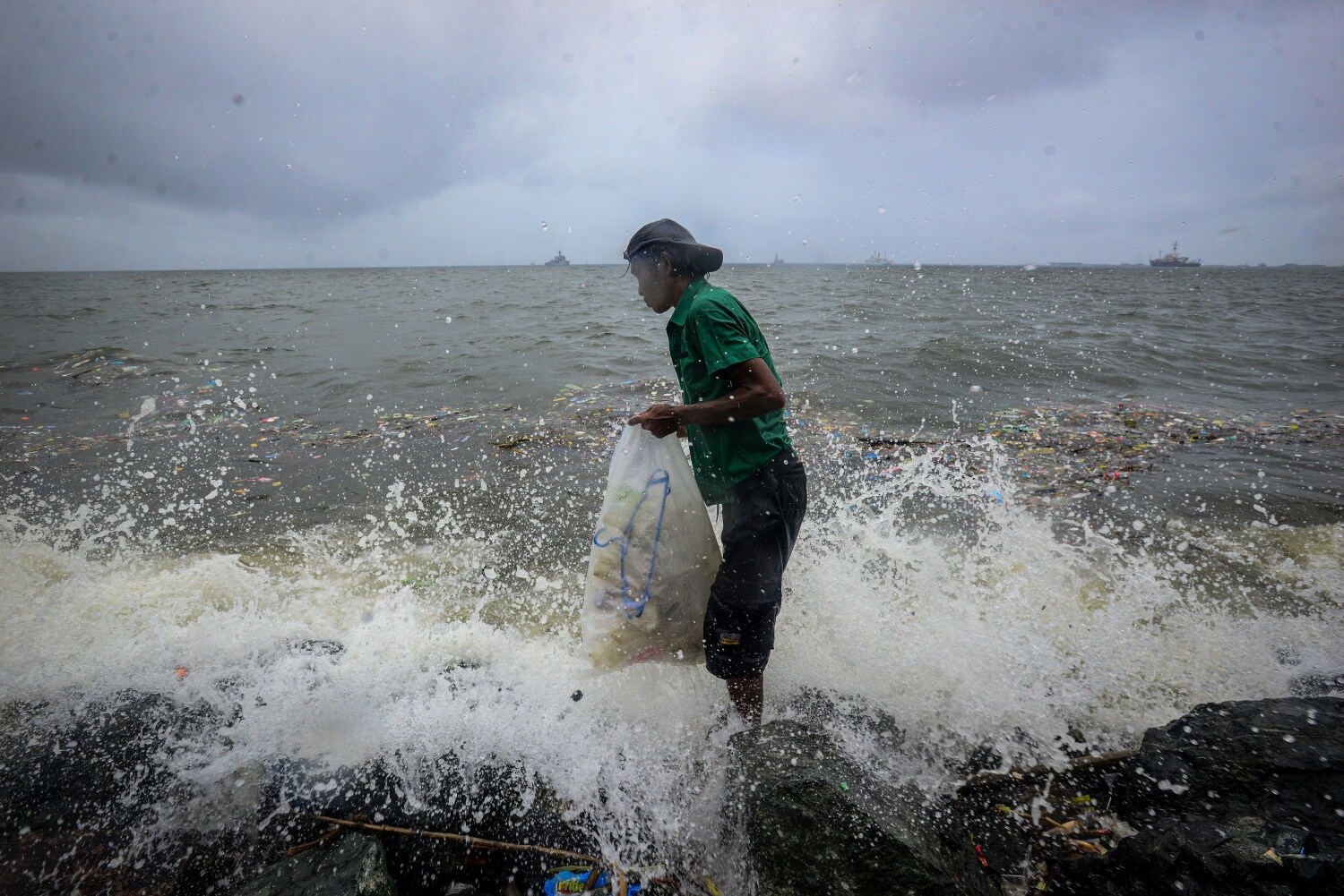 Un hombre recoge basura plástica de la bahía de Manila a pesar de la lluvia y las olas mientras las lluvias monzónicas afectan la ciudad.
