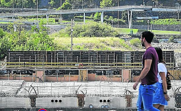 Dos jóvenes pasan ante las piezas apiladas del puente junto al canal de Deusto.