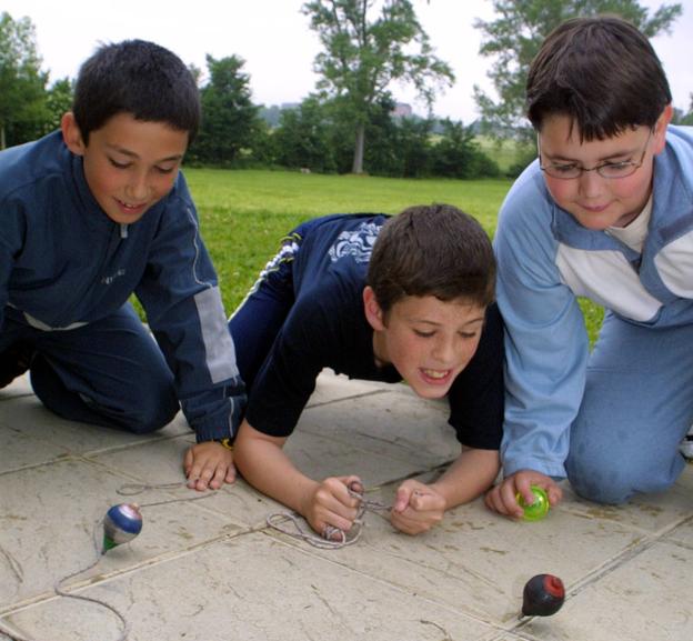 Unos niños juegan con peonzas.