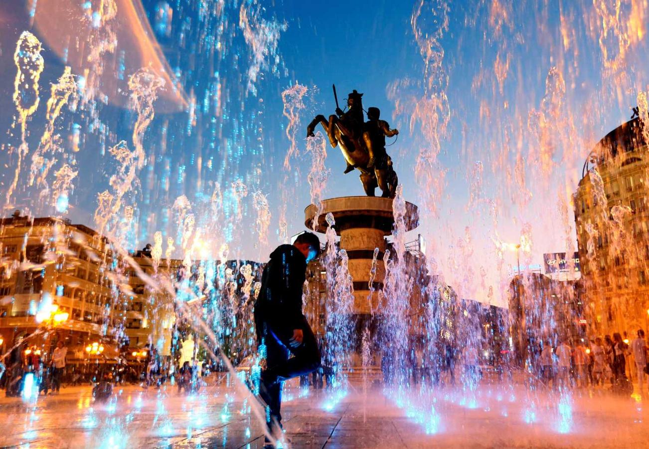 La gente juega con agua de una fuente cerca del monumento "Guerrero a caballo" en Skopje, Macedonia del Norte