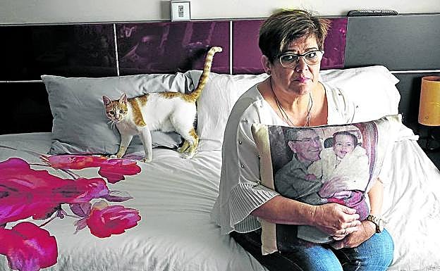 Ángeles Lozano, sentada en la habitación en la que pasó sus últimos días su esposo, abrazada a un cojín con su imagen y la nieta de ambos, en brazos. 