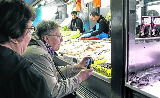 Una turista saca un primer plano de dos merluzas en una pescadería del Mercado de la Ribera.