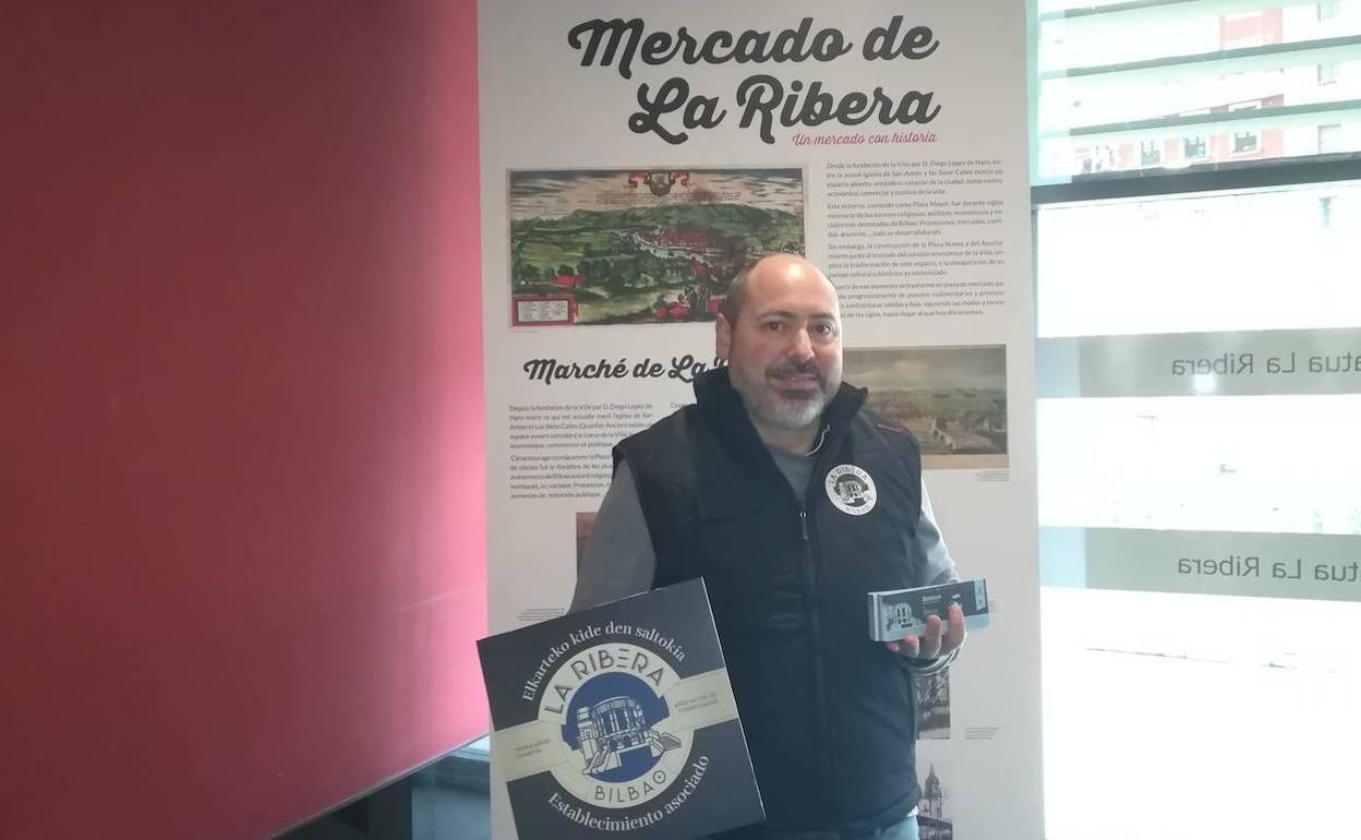 Asier Beato, presidente de la Asociación de Comerciantes del Mercado de la RIbera con el cartel de la agrupación y los bonos