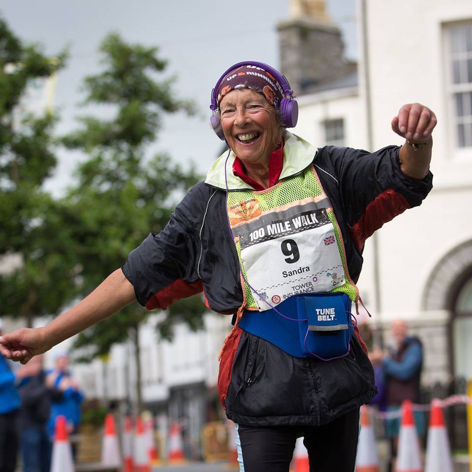 Sandra Brown, 70 años. andra Brown ha competido en más carreras de 100 millas que cualquier otra persona, hombre o mujer (en 205) y la única persona que ha competido en una carrera centurión. A su marido, Richard Brown, también corredor, le complace ser eclipsado por los logros de Sandra. “A la edad de 70 años Sandra Brown tiene tantos récords en el mundo de la ultra distancia que es realmente difícil saber por dónde empezar. En marzo, se convirtió en la primera persona en completar 200 eventos de 100 millas o más en la carrera de Dublín a Belfast, estableciendo un nuevo récord de 21 horas, 15 minutos y 33 segundos. La fotografié en la carrera de 100 millas Centurion de la Isla de Man en agosto, donde más de la mitad de los competidores abandonaron durante la noche húmeda, ventosa y fría. Hasta que se detuvo por enfermedad, Sandra había sido la mujer principal y perseveró para cruzar la línea como la segunda mujer en llegar (y en undécimo lugar en general). Había jóvenes de 20 años compitiendo, no era una carrera de veteranos. No paraba de sonreír. Mirándola en acción, no puedes evitar sentirte tocada por su magia. Ella es una verdadera leyenda en el mundo del ultrawalking y fue un verdadero privilegio haberla visto en acción”, revela Alex Rotas.