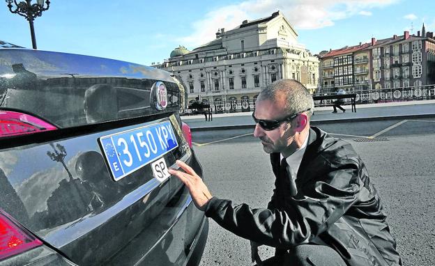 Un conductor de Uber limpia su vehículo, con el Teatro Arriaga de fondo.