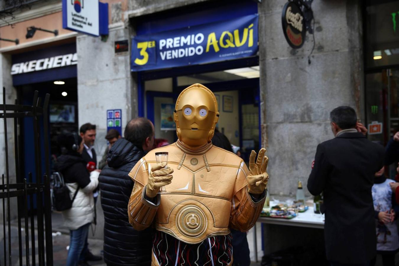 Una persona disfrazada del robot de la Guerra de las Galaxias C-3PO celebra en la administración de lotería 150 en la calle Arenal de Madrid 