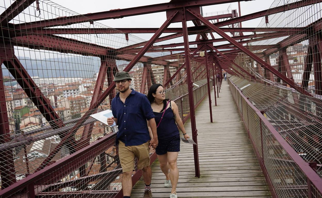 Una pareja de turistas camina por la pasarela del Puente Colgante. 