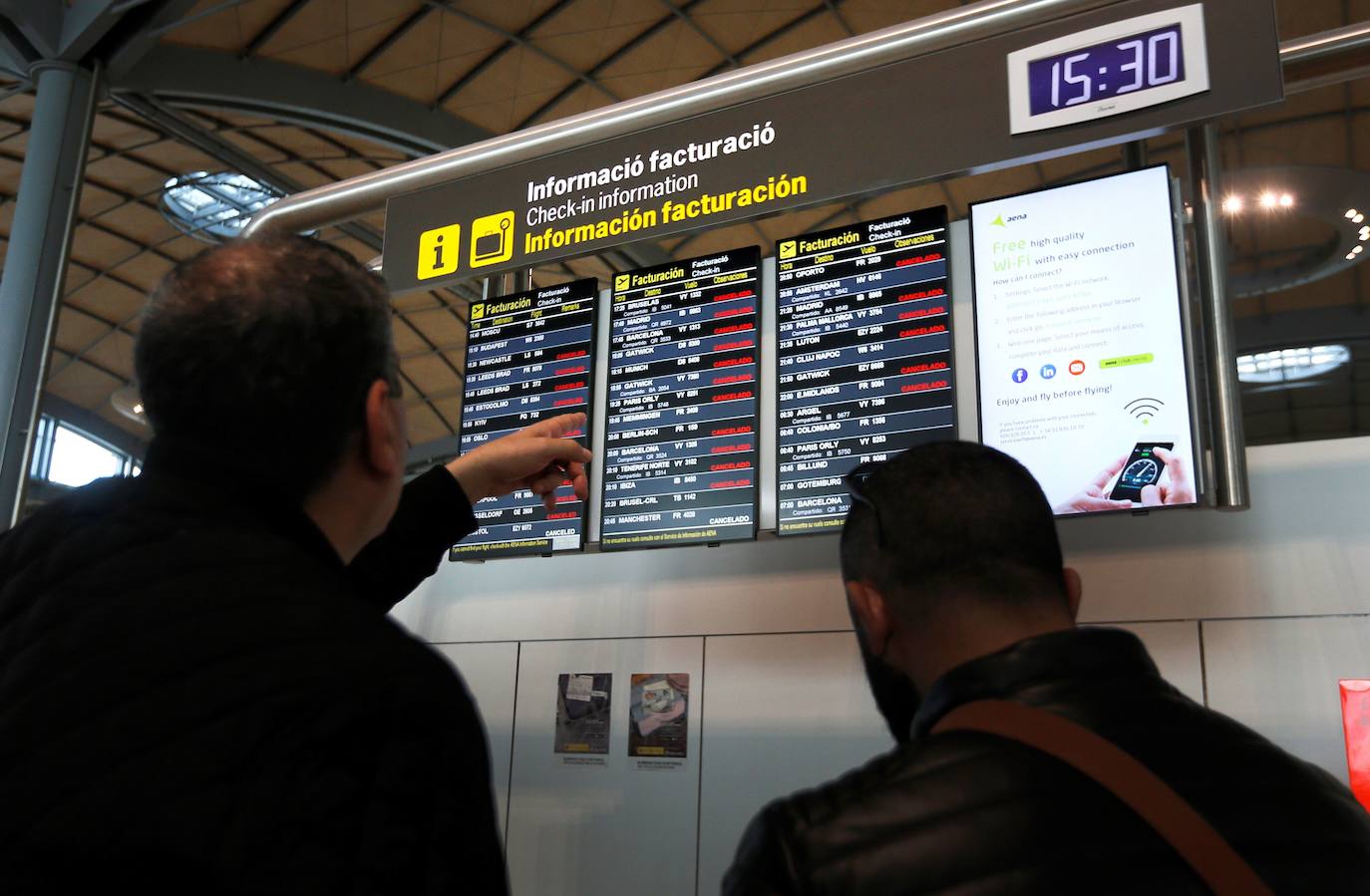 Dos viajeros miran un panel tras el cierre por precaución a causa de la borrasca Gloria del aeropuerto de Alicante-Elche