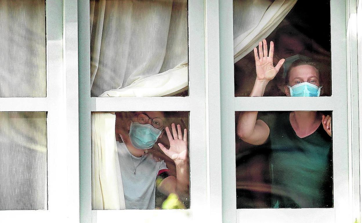 Turistas recluidos en el hotel de Tenerife sometido a cuarentena miran por la ventana protegidos con mascarillas. 