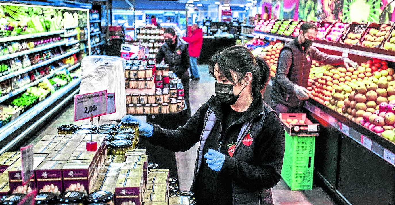 Empleados de un establecimiento de alimentación en la Avenida de Gasteiz reponen productos protegidos con guantes y mascarillas.