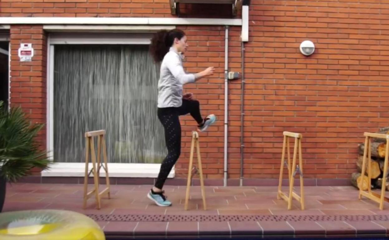 La atleta haciendo el gesto de saltar la valla con varios caballetes en su casa. 