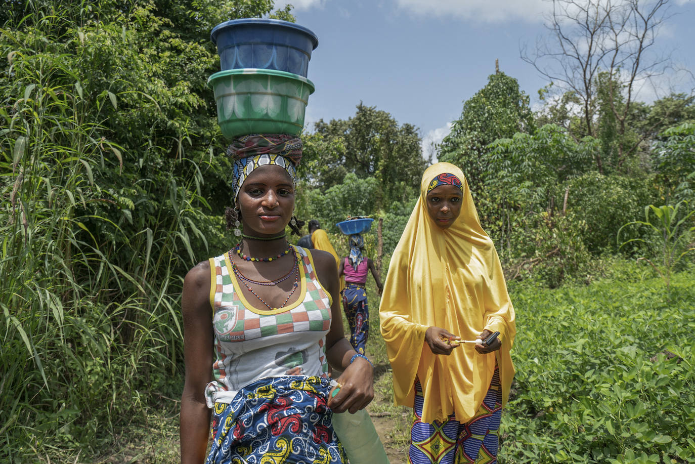 Mujeres de la etnia Fulani, ataviadas con ropas de vivos colores, deján atrás el campamento donde se levantan sus chozas para lavar la ropa en el río.