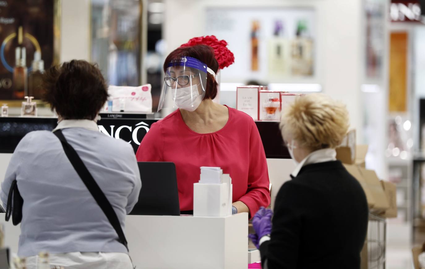 Una empleada potegida con mascarilla y visera atiende a los clientes del Corte Inglés de Bilbao. / Efe