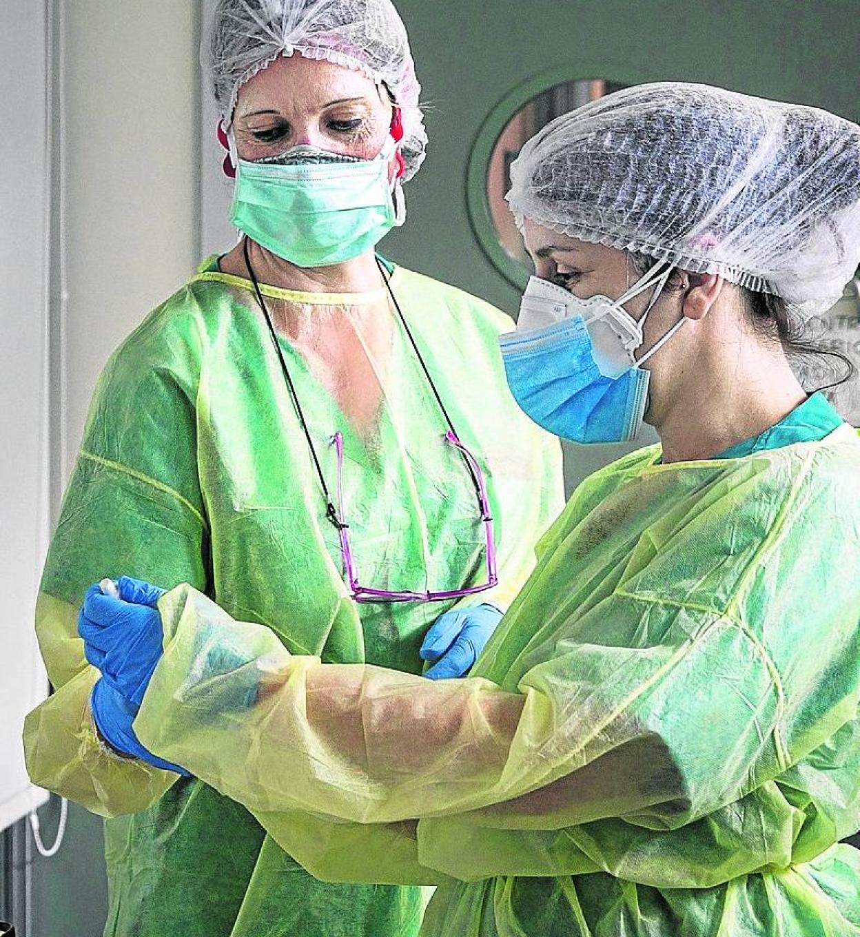 Dos sanitarias se colocan los equipos de protección individual. 