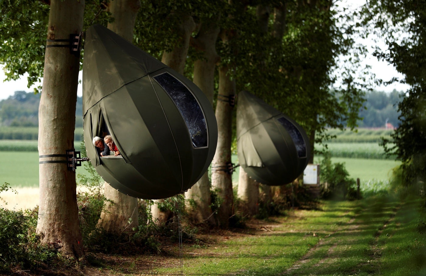 Huéspedes posan y se sientan dentro de una carpa en forma de lágrima que cuelga de un árbol creado por el artista holandés Dre Wapenaar, que ofrece un alojamiento inusual para turistas en el campo belga, cerca de Borgloon, Bélgica.