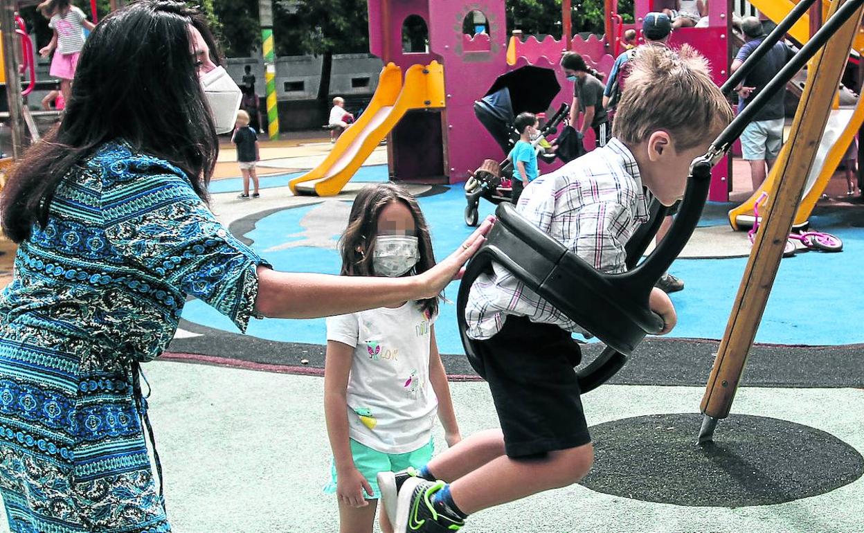 Una madre columpia a su hijo en un parque lleno de niños en Bilbao. 