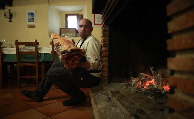 Jorge López sostiene una cita de chuleta junto a la chimenea de Valderejo Etxea.