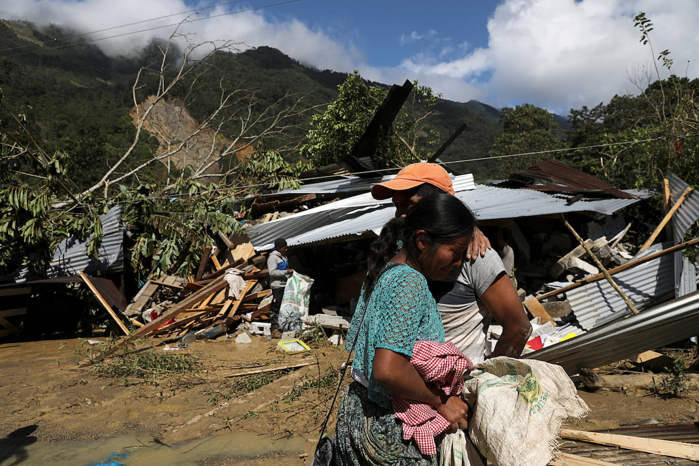 Gaspar Cal y su hija Leticia se abrazan de pie frente a su casa, dañada por un deslizamiento de tierra causado por las fuertes lluvias traídas por la tormenta Eta, mientras continúa la búsqueda de víctimas en el pueblo enterrado de Queja.