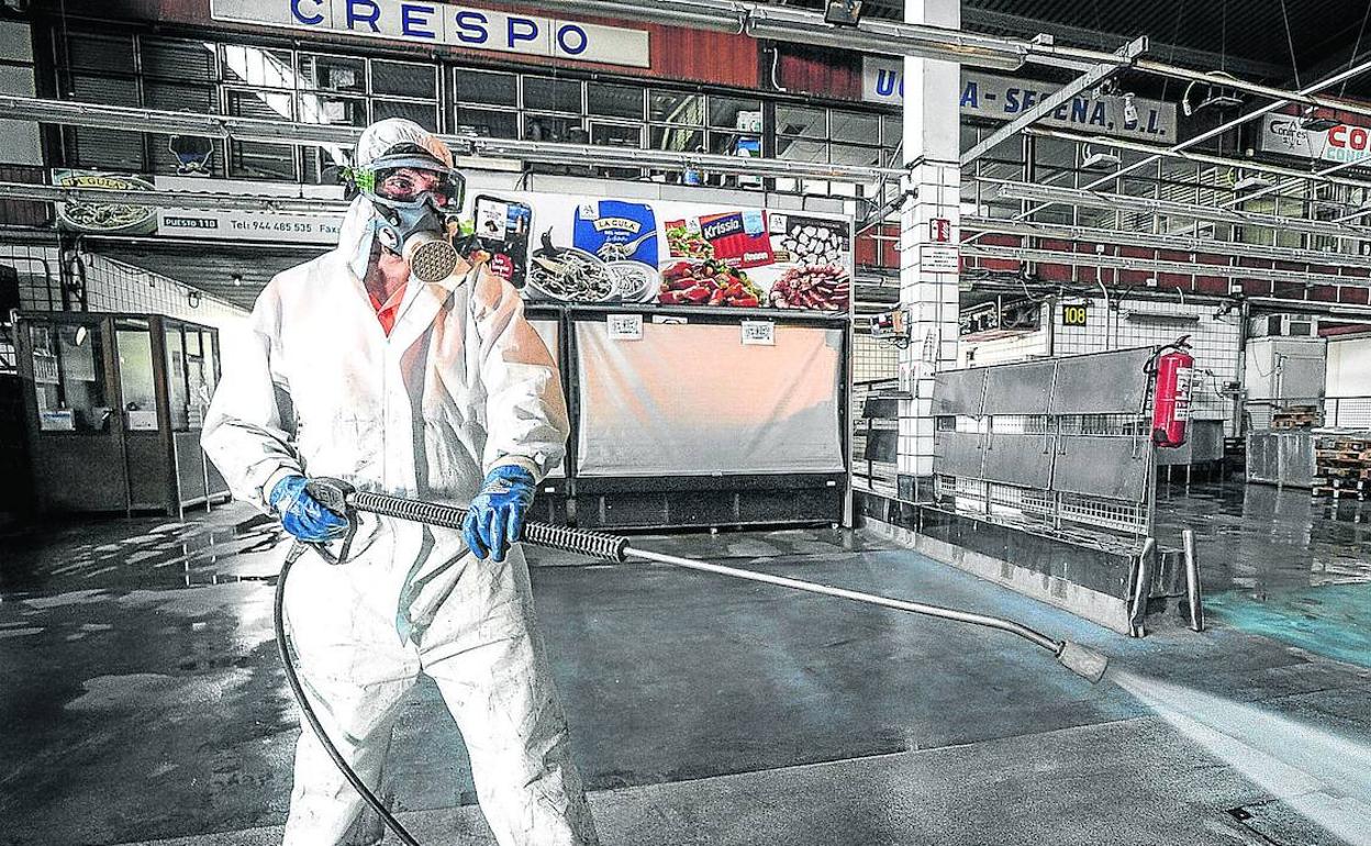 Un operario, equipado con un equipo completo de protección, desinfecta la superficie del pabellón del pescado en Mercabilbao cuando ya ha concluido la venta. 