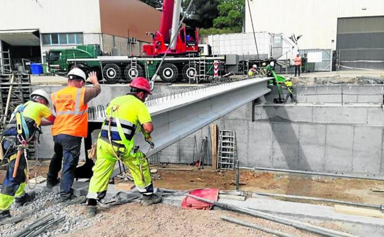 Dos trabajadores colocan una de las viguetas de un puente sobre el río Asua a su paso por Sondika.