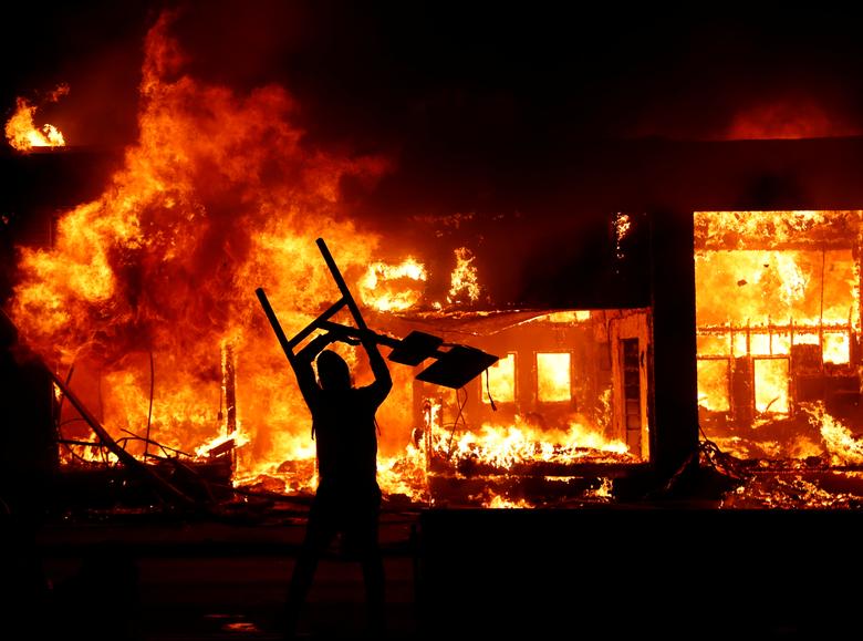 Un manifestante sostiene un objeto frente a un incendio durante una manifestación.