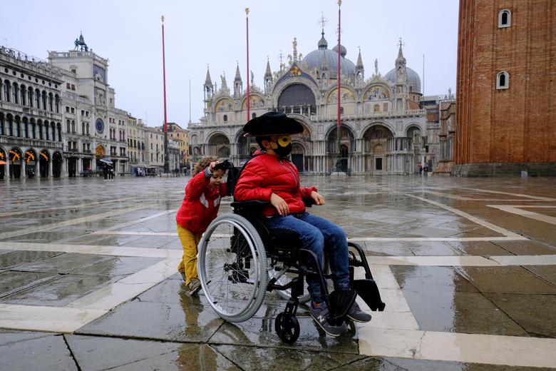 Un niño juega con la silla de ruedas de su abuela en la plaza de San Marcos mientras la gente celebra el carnaval anual de Venecia, que ha sido cancelado este año debido a la pandemia de coronavirus.