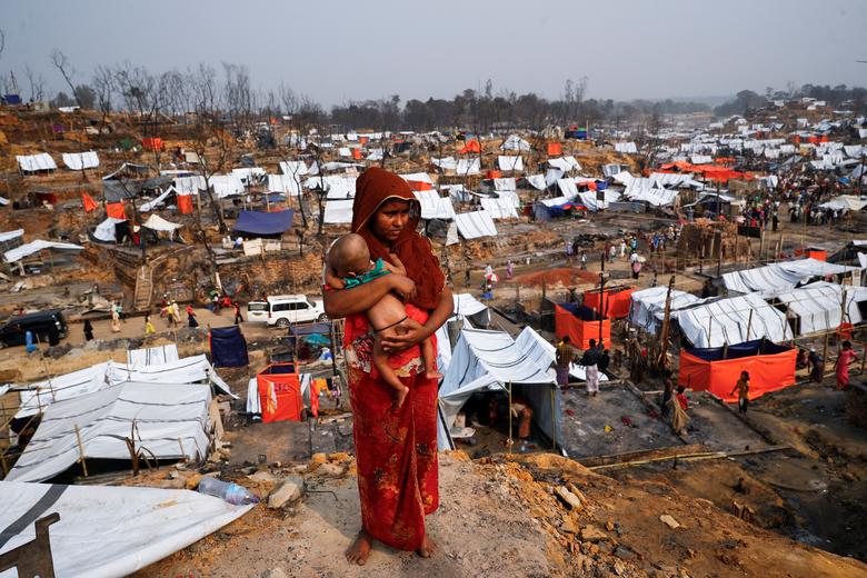 Una refugiada rohingya carga a su hijo mientras mira en un campo de refugiados después de un incendio masivo en Cox's Bazar.