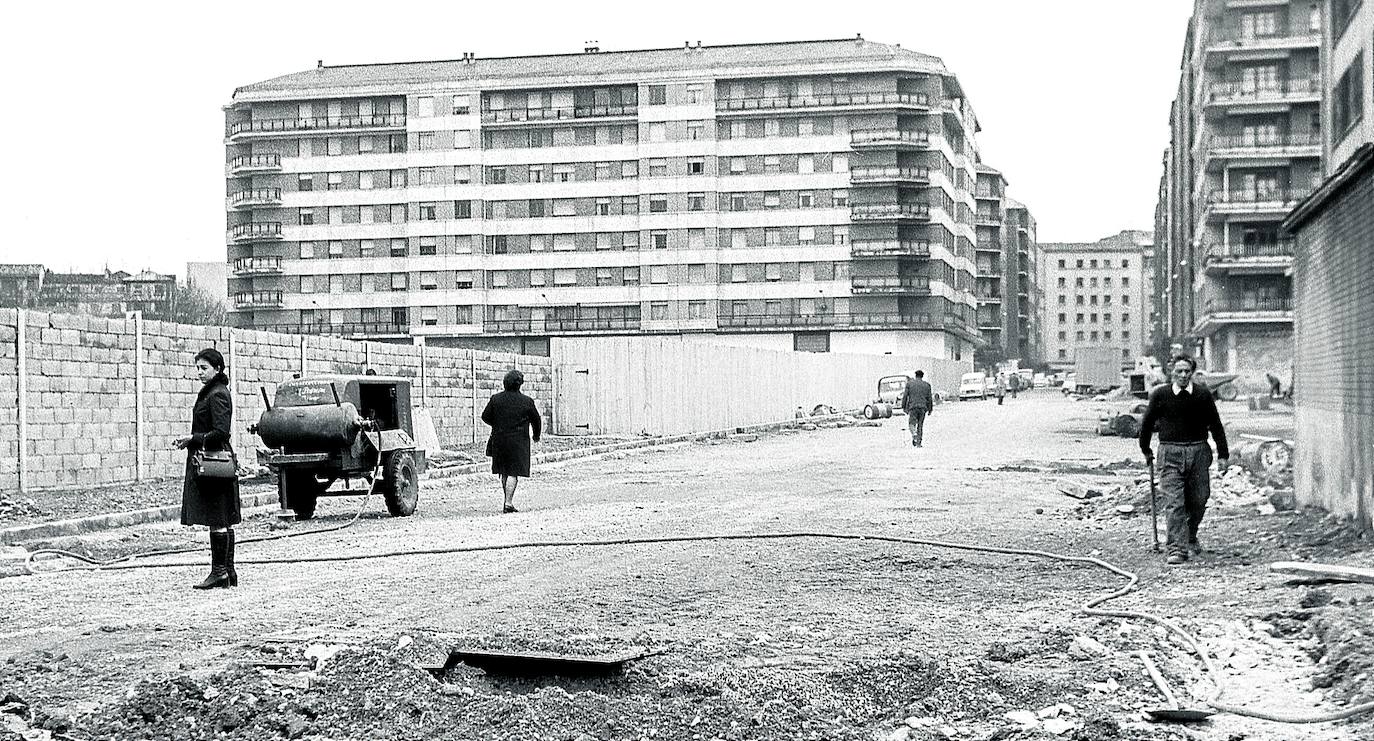 El llamado polígono de Desamparadas, que adoptó el nombre del convento de las Oblatas y la posterior iglesia de Nuestra Señora de los Desamparados, se organizó de acuerdo a un plan parcial de ordenación urbana diseñado por el arquitecto Enrique Marimón. Aprobado el 25 de enero de 1969, planteaba la consolidación de un barrio residencial con un gran espacio público en el centro, una plaza con parque y jardines. Derribada la cárcel de la calle La Paz y los cuarteles del regimiento de Artillería -en sus últimos años, del batallón de Ingenieros- se liberó un inmenso solar, un espacio que dio para construir viviendas, crear la plaza de Santa Bárbara, reubicar la Plaza de Abastos y acoger el primer gran centro comercial de la ciudad, Galerías Preciados, hoy El Corte Inglés. Se prolongó la calle Postas hasta la de Los Herrán al desaparecer la prisión y también se abrió el segundo tramo de Jesús Guridi, de Pío XII hasta La Paz, el que se aprecia en la imagen en fase de urbanización, tomada en febrero de 1972. Más allá de las tapias, primero se levantaría el Nuevo Mercado de Abastos Municipal, proyecto de Ángel Esteve aprobado en marzo y construido por Olabarría Hermanos con un presupuesto de 82 millones de pesetas. Y después, entre febrero y junio de 1975, se presentó el boceto de Enrique García para la edificación de los grandes almacenes. 