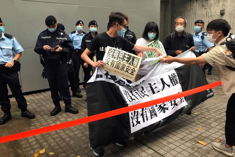 Figo Chan, Chow Hang-tung y otros activistas prodemocráticos sostienen una bandera y pancartas junto a los agentes de policía y miembros de los medios de comunicación durante una manifestación contra el Día Nacional de Educación sobre Seguridad en Hong Kong.