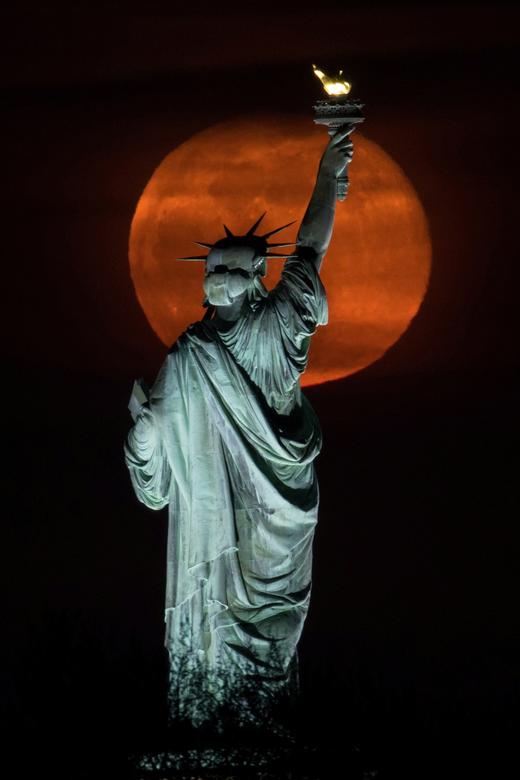 La luna llena, conocida como Super Pink Moon, se eleva detrás de la Estatua de la Libertad en la ciudad de Nueva York.