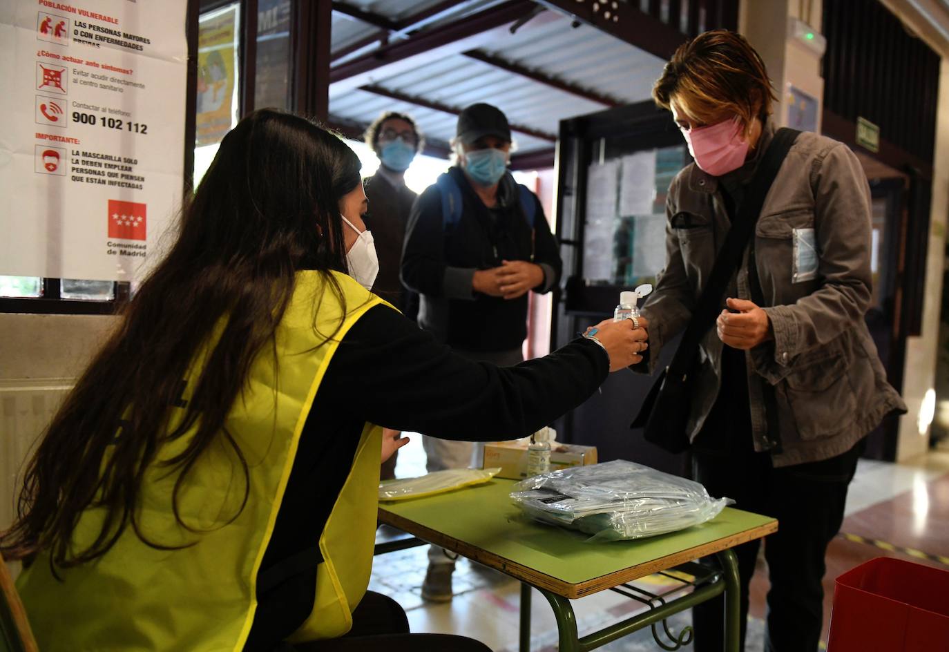 Una mujer ofrece gel hidroalcohólico a los votantes que acuden al colegio Roma de Madrid.