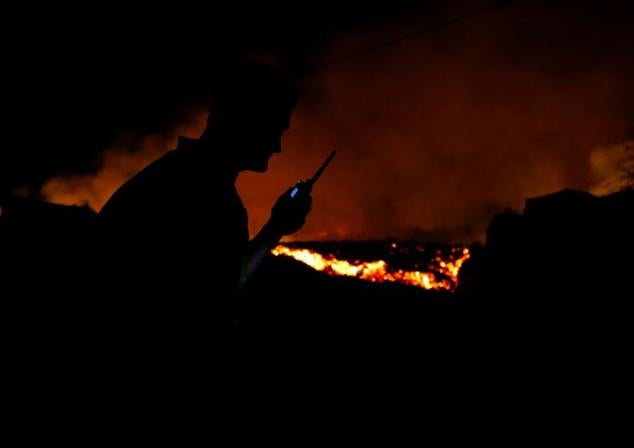 La lava fluye junto a un policía local tras la erupción del volcán.