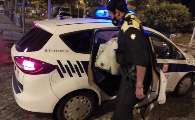 Un agente guarda las botellas incautadas a unos jóvenes. 