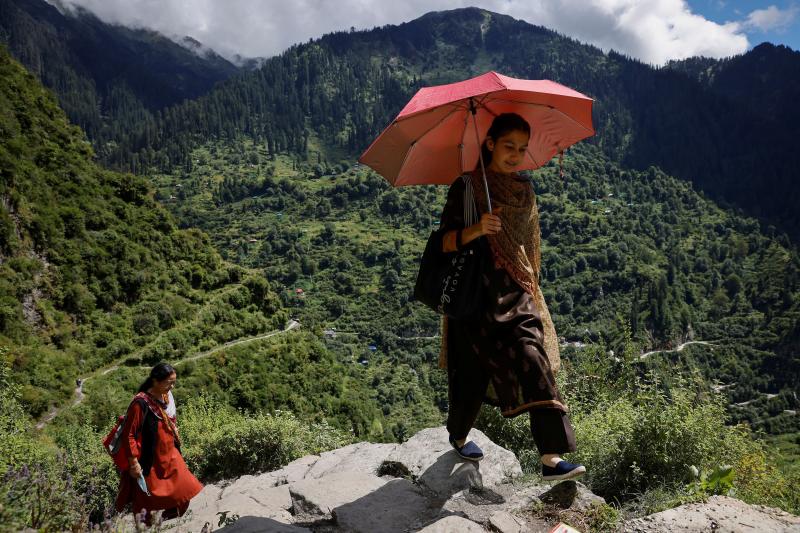 Las sanitarias Kamla Devi, de 58 años, y Kanta Devi, de 26, caminan por el terreno, muy escarpado, y se protegen del sol. Tendrán que hacer trekking durante horas antes de ponerse a vacunar.