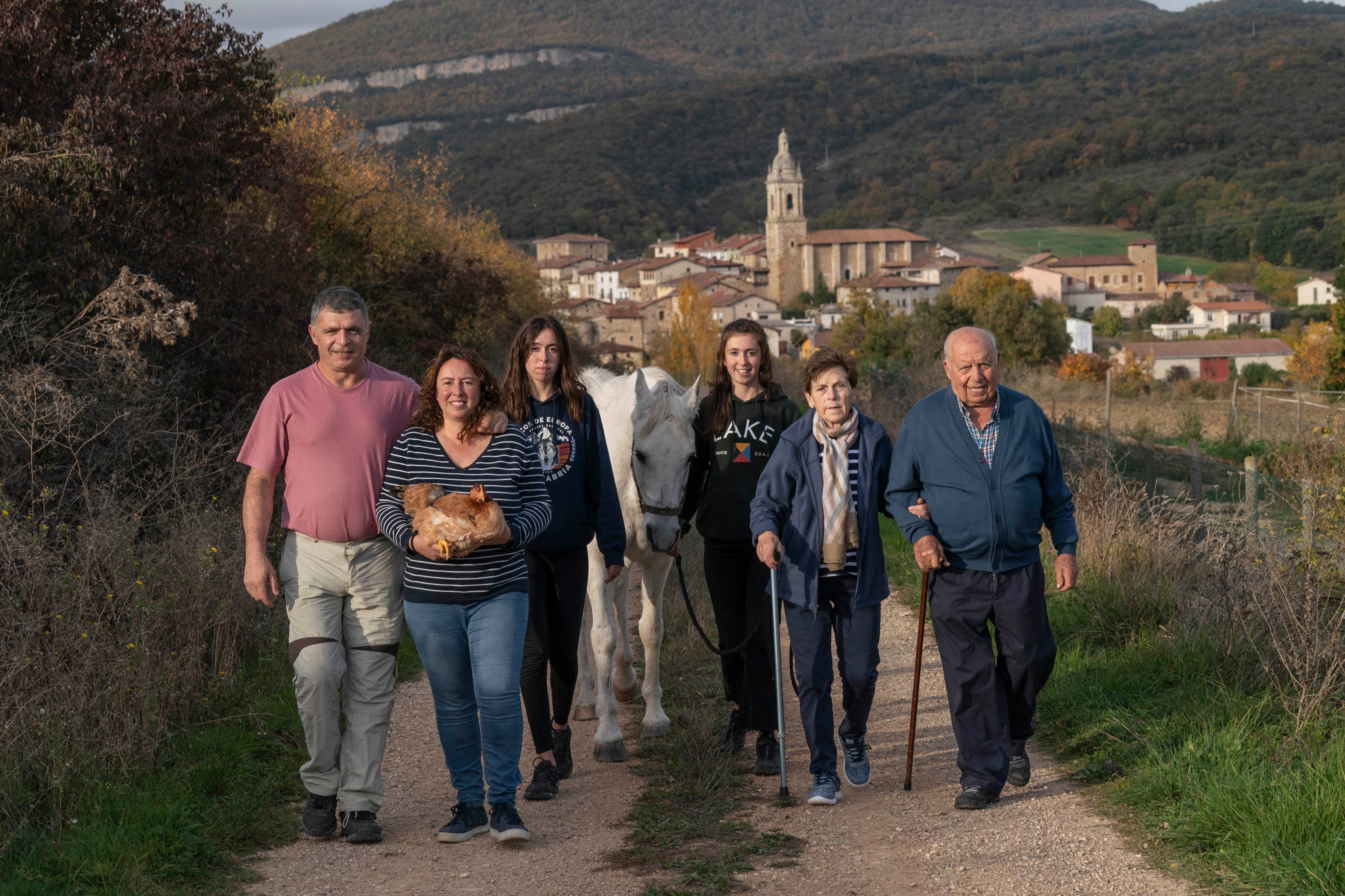 La familia a completo, con Kuki, el caballo blanco, camina por un sendero hacia sus fincas, con el pueblo a sus espaldas. 