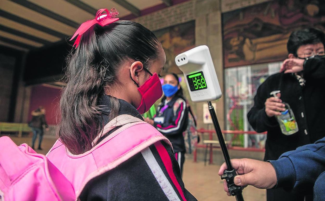 Un profesor toma la temperatura a una alumna para verificar su estado de salud, antes de entrar en un centro escolar. 