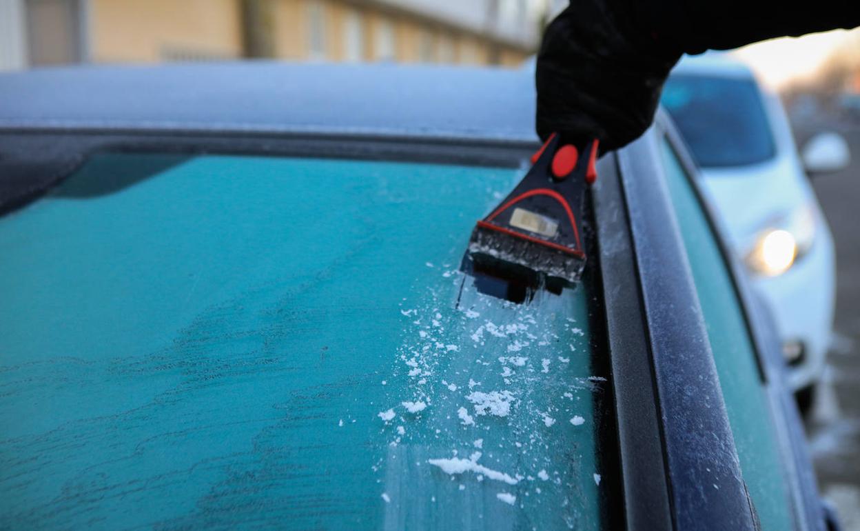 Un conductor retira la capa de hielo adherida a la luna de su vehículo.