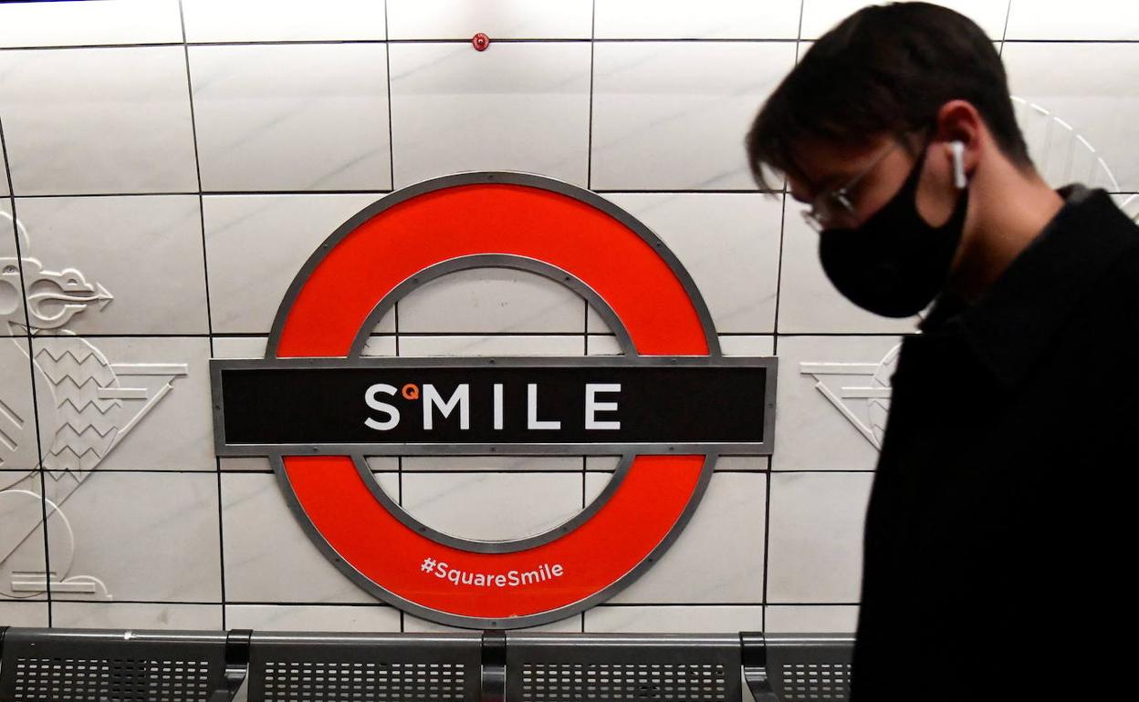 Un hombre pasa junto a un cartel que dice 'Sonríe' en el metro de Londres.