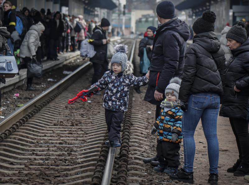 Unos niños ucranianos y sus familiares esperan sobre la vía del tren la llegada del tren en la estación de Kiev.