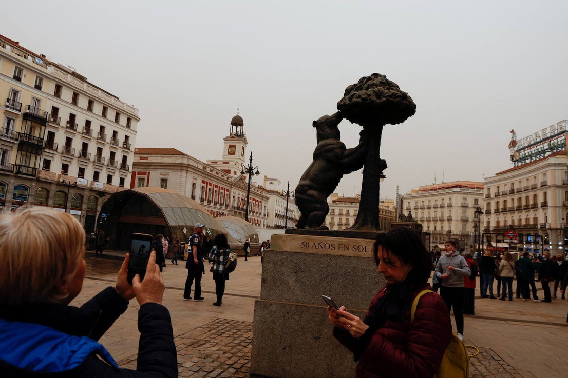 Una persona hace una foto a la estatua del Oso y el Madroño subierto de arena, en la Puerta de Sol de Madrid.