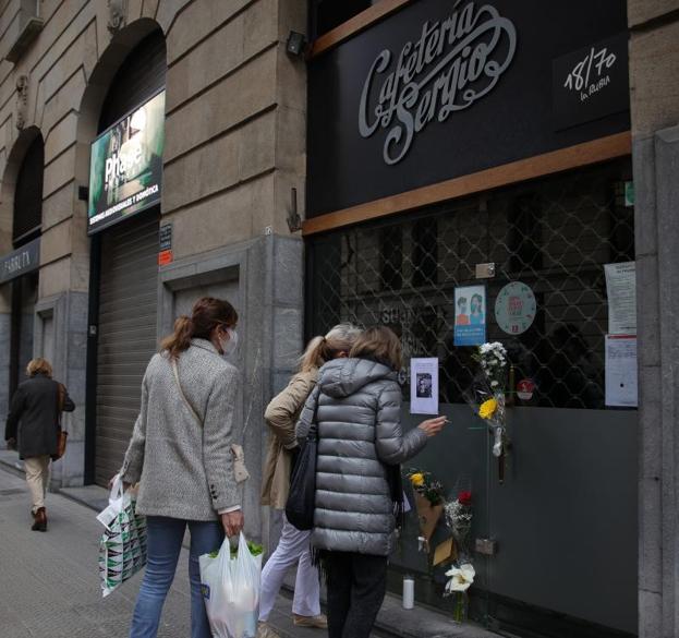 Unas mujeres leen los mensajes puestos por los clientes en la cristalera, junto a ramos de flores.