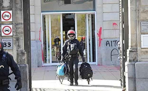 Un ertzaina traslada un par de mochilas incautadas a los jóvenes arrestados.