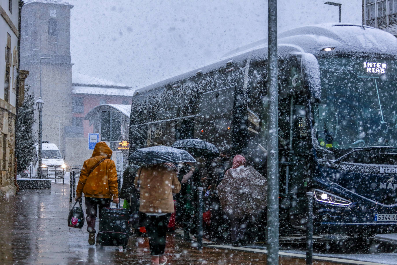 Vecinos de Murgia se protegen de la nieve mientras suben a un autocar.