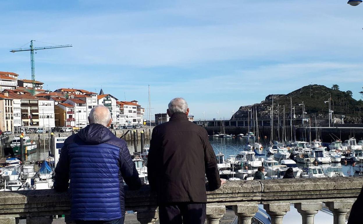 Dos personas mayores miran al puerto de Lekeitio desde la plaza de la localidad turística. 