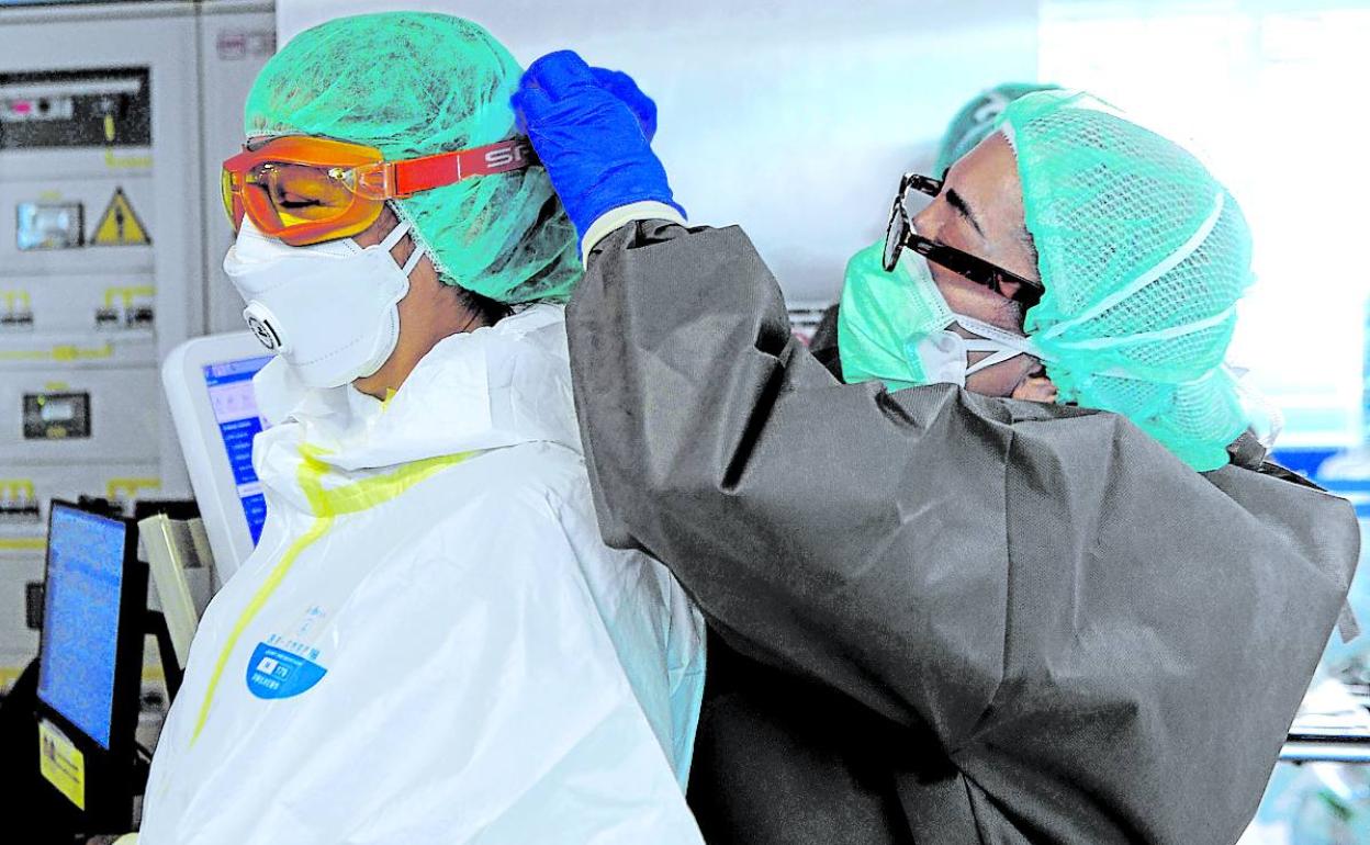 Una sanitaria ayuda a una compañera a colocarse las gafas en una UCI con pacientes covid. 