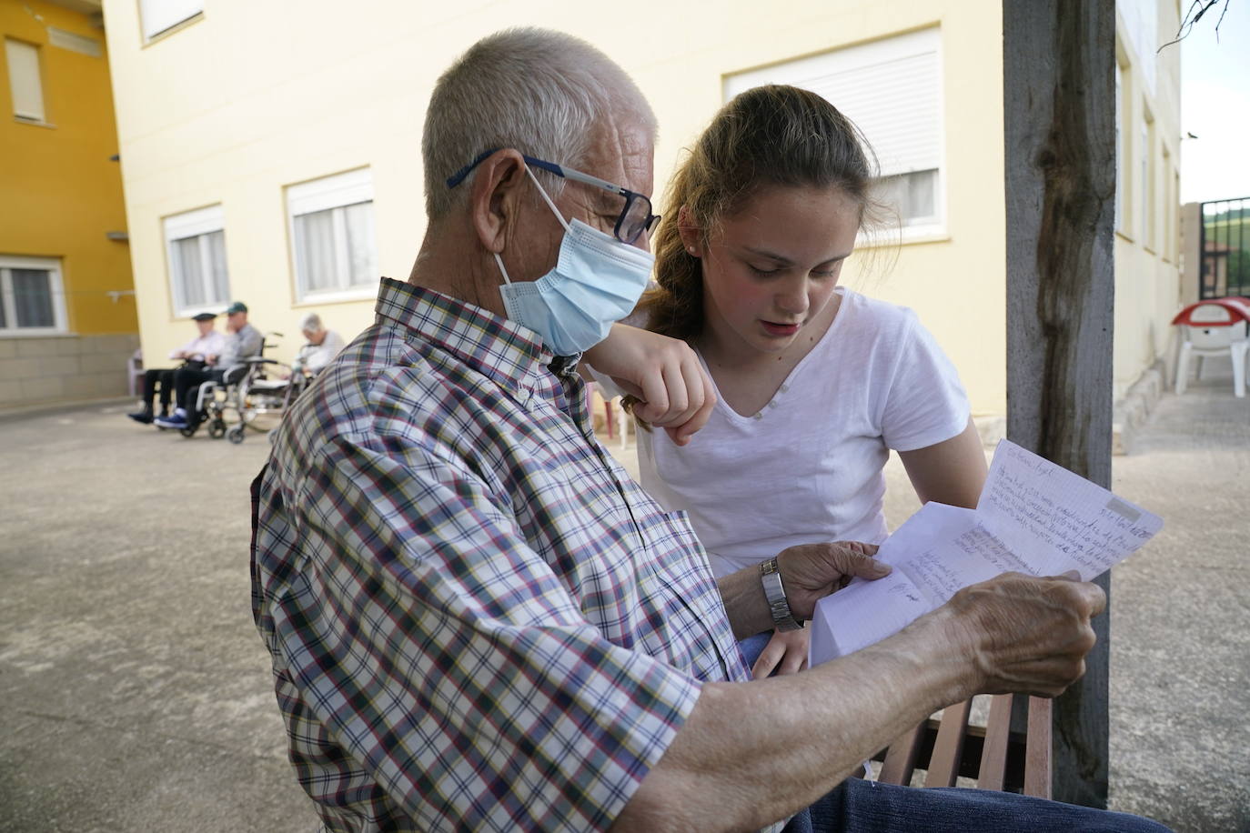 Una persona mayor y una chica, ajenos a esta información, leen una carta en una residencia. 