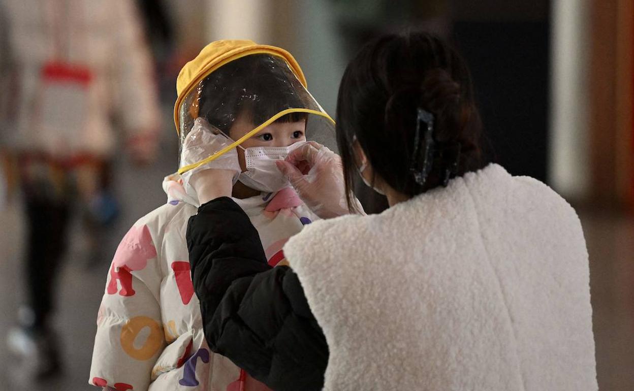 Una madre coloca bien la mascarilla a su hija en un aeropuerto chino. 