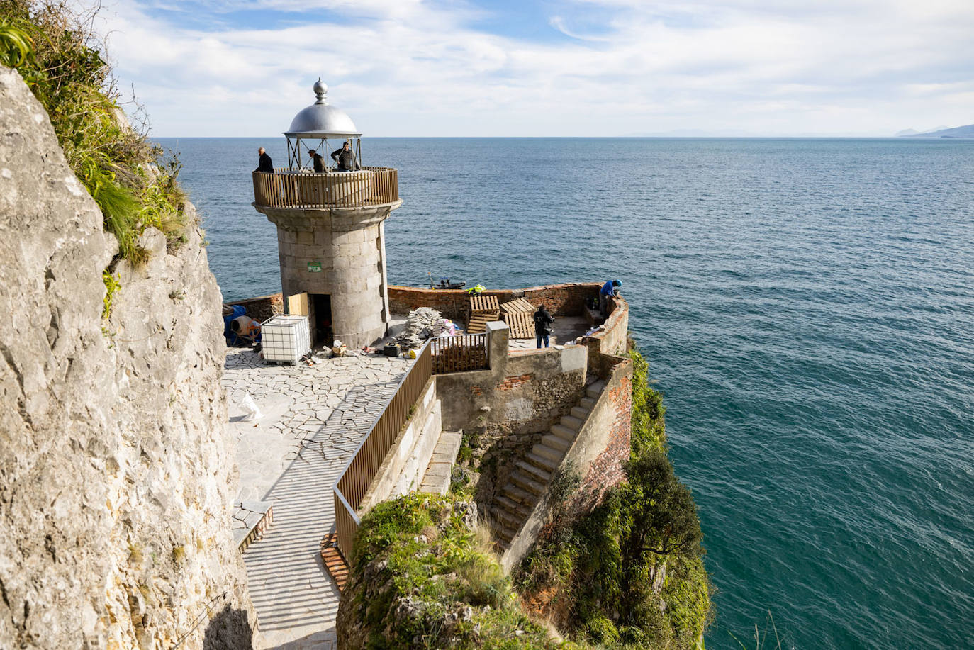 Dos operarios trabajan en la mejora del firme del área del faro con el alcalde, Sergio Abascal, observándoles desde la torre.