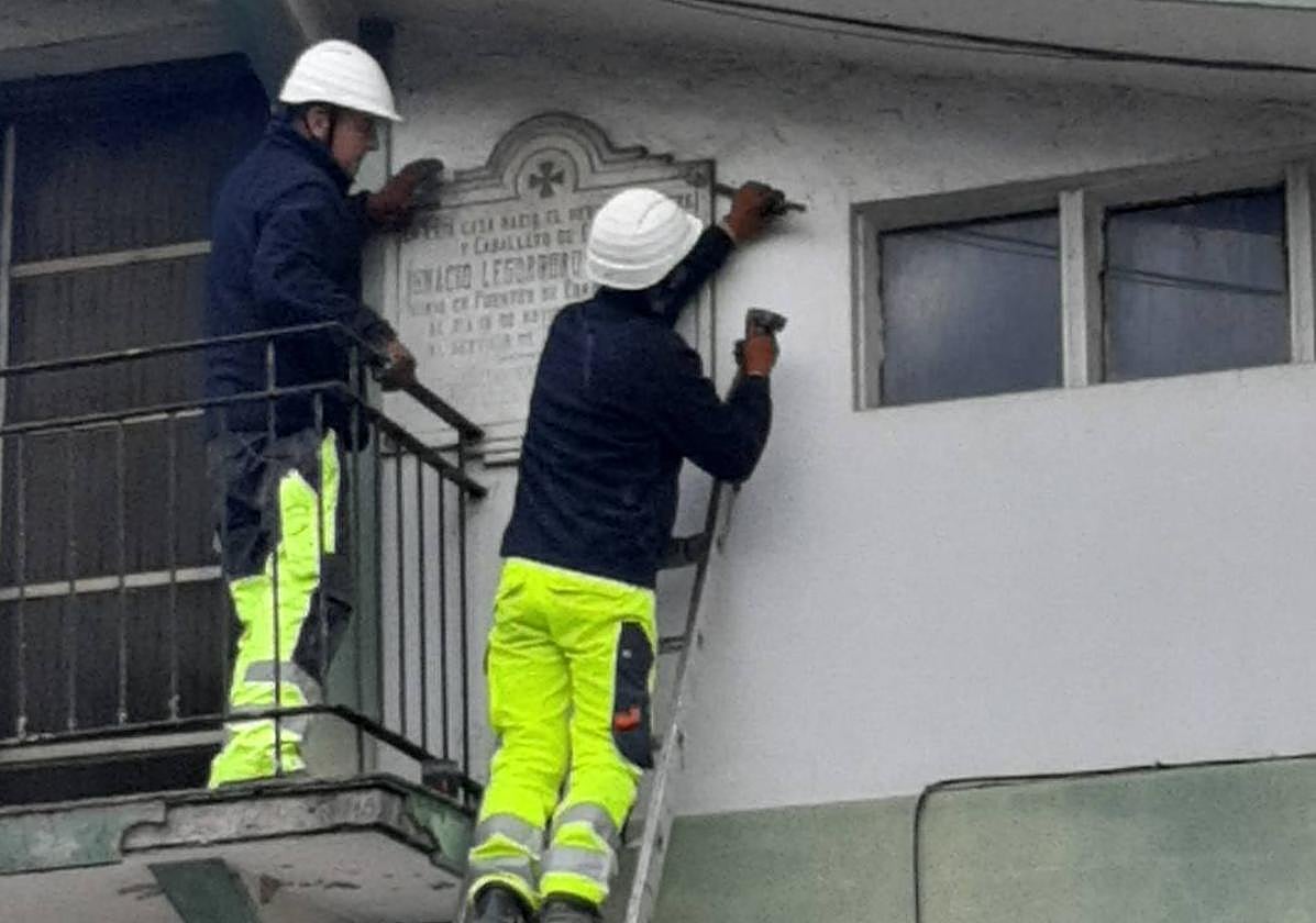 Operarios retiran la placa de la fachada de la vivienda