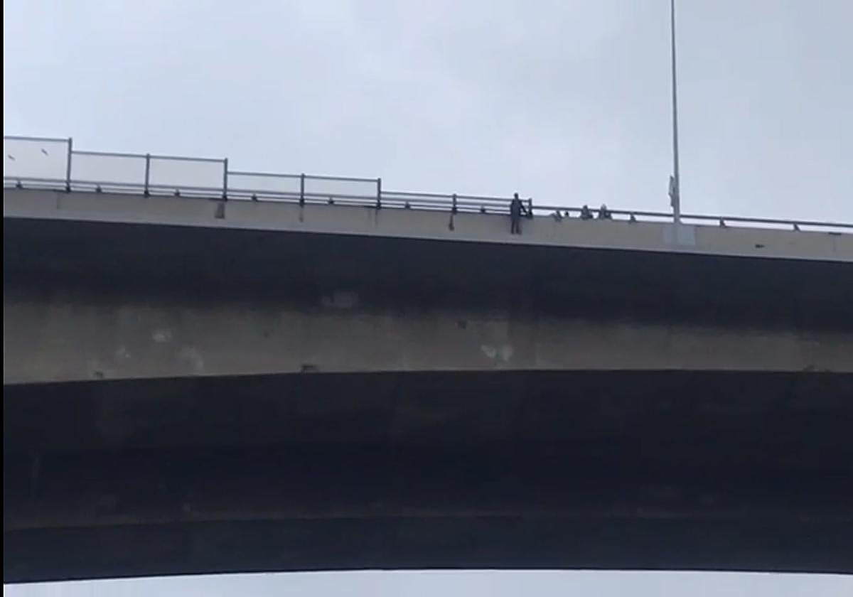 El hombre, agarrado a la valla del puente con el cuerpo hacia afuera.